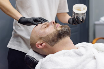 Fototapeta premium beard modeling in Barber shop, beard care for men, male beauty and care concept, applying the scrub to the face