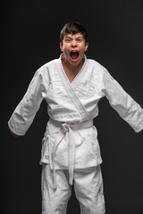 Fototapeta na wymiar a teenager dressed in martial arts clothing posing and crying on a dark gray background, a sports concept