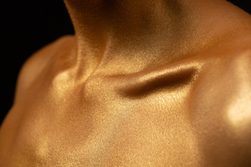 in gold paint a man. Shiny clavicle detail photo. Shiny body art paint gold on a black background.