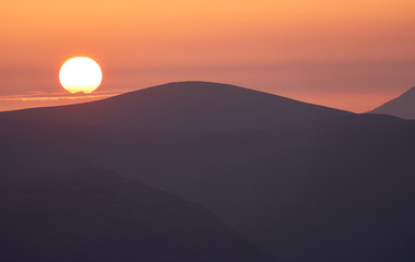 Late evening glow of sunset over the mountains of the Lake District with the sun just about to dip below the ridgeline.