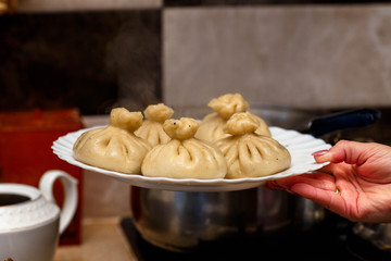 cooked khinkali on a white Cup in the hands of a girl in a green apron