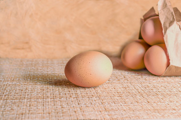 One raw egg in front and three in paper package behind on a light background