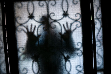 Figure of mysterious stranger pressing hands against a textured glass door with security bars