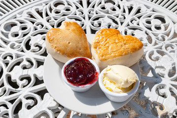 Pair of fresh heart-shaped English scones sitting together outdoors on a sunny decorative table...