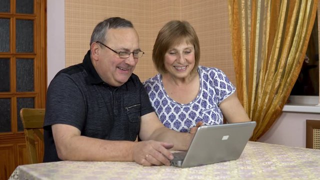 A man and a woman communicate with friends via video communication through a laptop. An old man and an old woman communicate and wave their hands while looking into a laptop. The family is sitting in