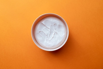 Open jar with face or body cream on an orange background. Skin care, beauty concept.