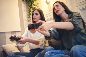 Two teenage girls playing games in the room, having fun and relaxing.