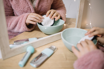 Girl's hands putting cotton pad in a bowl with a lotion