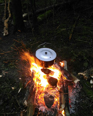 Bowler hat hands over a campfire on summer evening. Hiking trip in a forest.