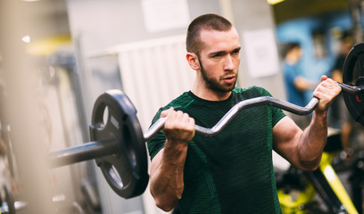 Young fitness man doing barbell curl in gym