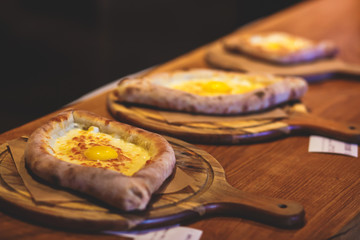 Process of cooking traditional adjarian georgian and armenian cuisine, hachapuri khachapuri with suluguni cheese and egg yolk on a wooden table with chief's hands in the background