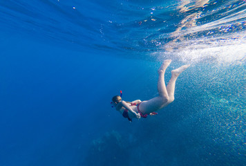 Obraz na płótnie Canvas Girl with a mask and a snorkel dives into the sea with corals and fish