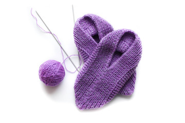 Handmade knitted pink slippers with knitting needles and ball of yarn. On white background you can easily place text or change the background