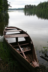 An old, half-sunken boat on the shore of a pond.