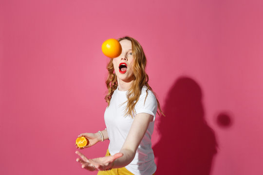 Orange fruits, healthy eating, true emotions - a young blonde woman juggling oranges on pink background - diet, people and mood concept.