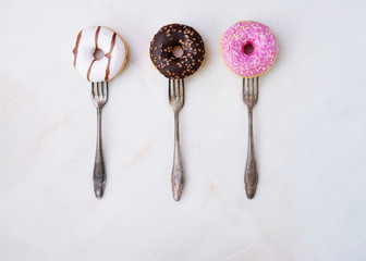 Glazed, chocolate frosted and sprinkled donuts on forks isolated on marble background. Top view....