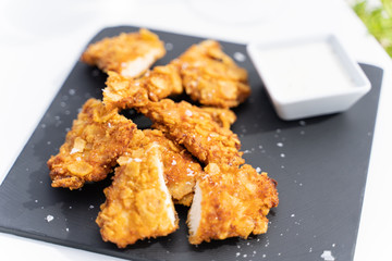 Fried chicken with salt served in a dark board with a small bowl of yougurt sauce