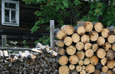 Firewood harvested for the winter is stacked near an old log house.