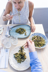 Vertical photo of a blonde girl eating veggie noddles with chopsticks