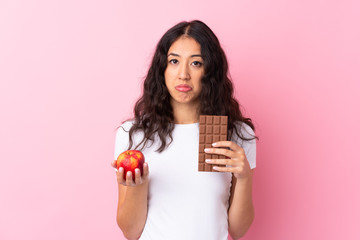 Spanish Chinese woman over isolated pink background taking a chocolate tablet in one hand and an...