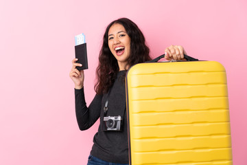 Mixed race woman over isolated pink background in vacation with suitcase and passport