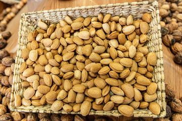 Close up of a basket of fresh, peeled almonds on sale at the local food market. Other dried fruits in the blurred background. Healthy snacks.