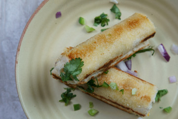 A stack of  toasted bread filled with a mixture of cheese, onion, peppers and cilantro on a plate.