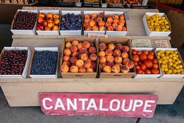 Close up neatly arranged cardboard boxes of bright orange apricots. Fresh plump fruit on sale at the local market and sign reading cantaloupe. Selective focus.