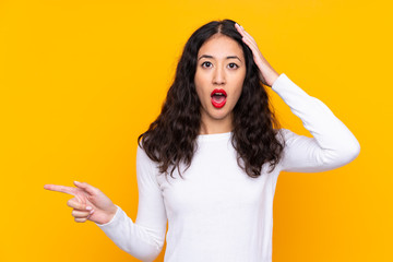 Mixed race woman over isolated yellow background surprised and pointing finger to the side