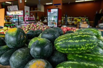 Close up shot of with fresh, oval or long shaped watermelons with dark green peel. Other fruits and beverages in the background. Local market ambient.