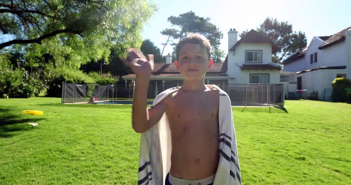 Child boy waving hello to camera with hand after swimming pool. Kid standing outside during summer day