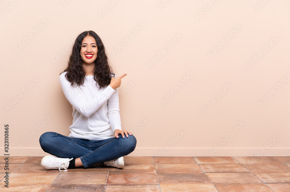 Wall mural young woman sitting on the floor pointing back