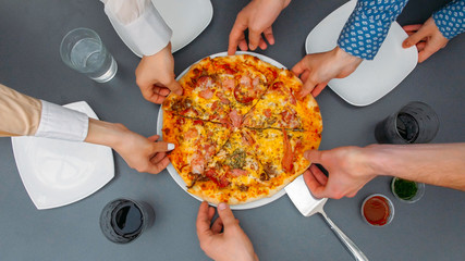 Hands taking pizza pieces from plate on table. Top view. People spreading arms to get slices of pizza. Group of hungry friends order fast food delivery.