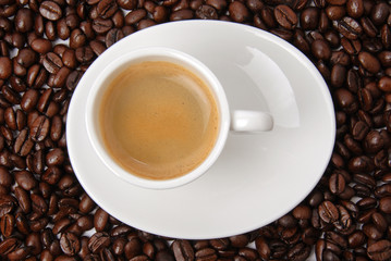 Cup of black coffee on coffee beans background. Hot aromatic americano or espresso cup on saucer. Top view.
