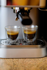 Coffee machine making, pouring fresh coffee into cups. Italian espresso coffee machine dispensing freshly brewed coffee into two glass cups. Process of preparation of coffee, closeup.