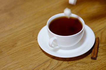 Classic white cup of black tea with saucer, teapot, sugar and cinnamon on the wooden table background. Breakfast drink at home or cafe.