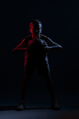 Fototapeta na wymiar Kid playing basketball isolated on black background in mixed light