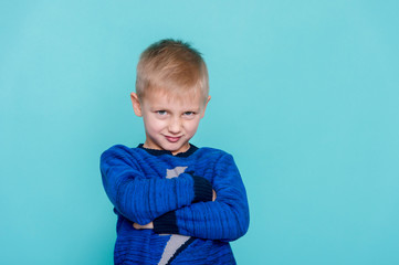 The little boy on a blue background was offended by folding her arms and frowning eyebrows