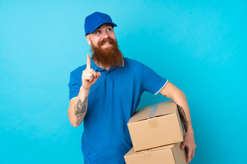Redhead delivery man over isolated blue background intending to realizes the solution while lifting a finger up