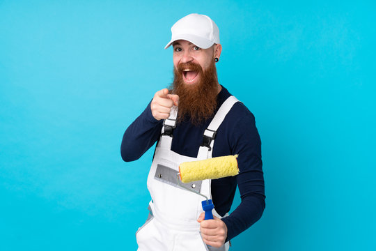 Painter man with long beard over isolated blue background points finger at you