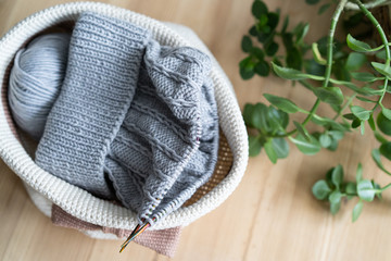 knitting from gray yarn, in a decorative basket crocheted on a wooden table