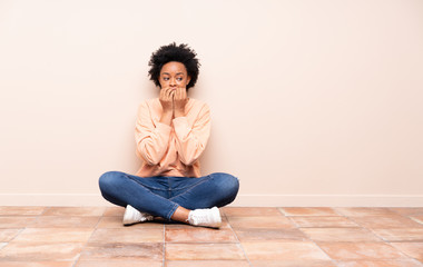 African american woman sitting on the floor nervous and scared putting hands to mouth
