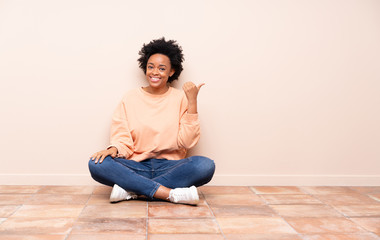 African american woman sitting on the floor pointing to the side to present a product