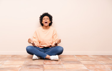 African american woman sitting on the floor shouting to the front with mouth wide open