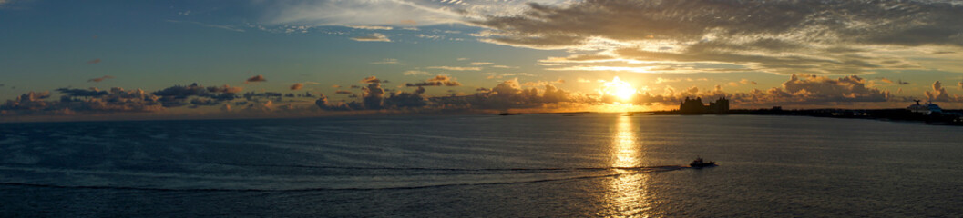 Naklejka na ściany i meble panorama, grateful sunrise over the ocean off the Bahama Islands with an orage sky, reflection on the sea and silhouettes of buildings in the background