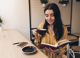 Obraz premium Pretty woman in urban cafe read book and drink black coffee