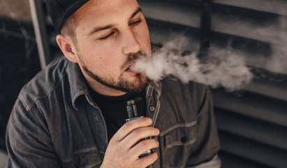 Young handsome man smoke with vape near black wall