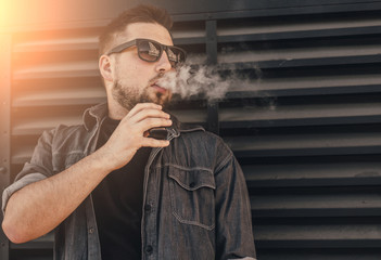 Young handsome man smoke with vape near black wall