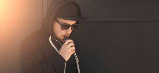 Young handsome man smoke with vape near black wall