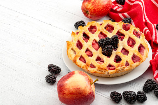 Homemade Sweets, Indulgence And Fruity Cakes Concept With Freshly Baked Tasty Warm Apple And Blackberry Pie, Raw Apples, Fresh Blackberries And Red Tea Towel Isolated On White Wood Rustic Background